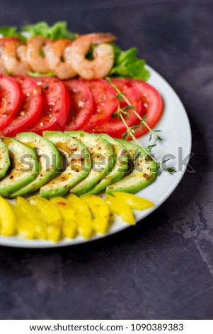 Avocado, tomato, pepper and shrimps on a plate lined with rows. Avocado salad on a dark background.