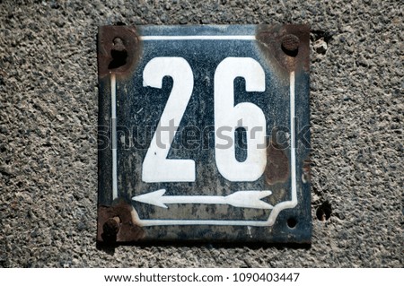 Weathered grunge square metal enameled plate of number of street address with number 26 closeup