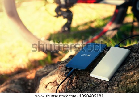 A portable charger charges the smartphone. Power Bank with cable against the background of wood and bicycle.