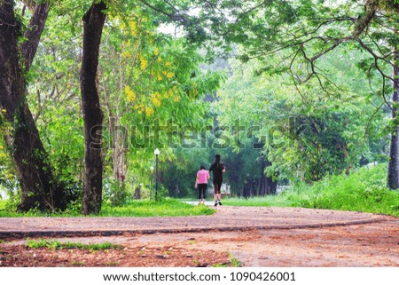 A front selective picture of a green natural park with a jogging woman. 