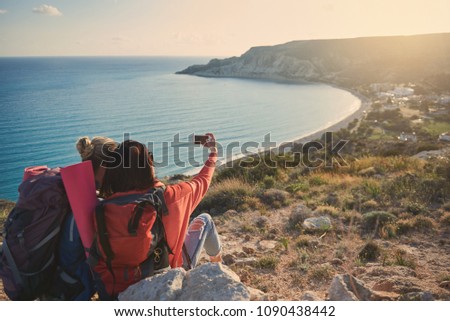 Two girls with backpacks sitting with their backs on mounting and photographing themselves. Copy space in right side