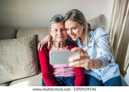 Elderly grandmother and adult granddaughter with smartphone at home.