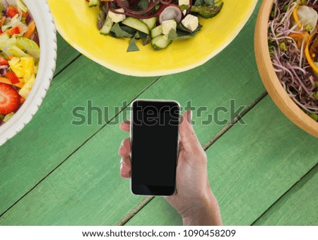 Person holding a phone against a green wooden table with food
