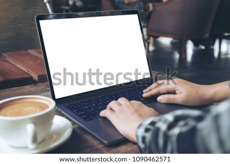 Mockup image of a businesswoman using laptop with blank white desktop screen with coffee cup on wooden table in cafe