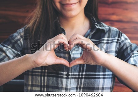 A smiley face Asian woman making heart hand sign with feeling inlove