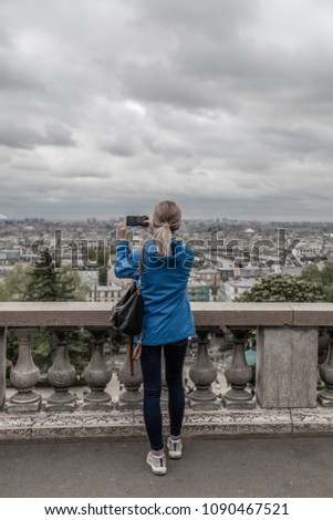 Woman tourist taking photo of the city in cloudy weather with mobile smart phone. camera.