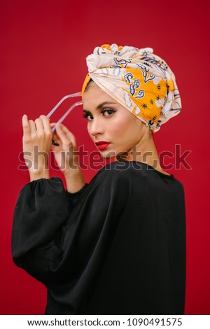 Fashion portrait of a beautiful, tall and fashionable woman of Middle Eastern descent. She is posing against a red, plain background.  Royalty-Free Stock Photo #1090491575