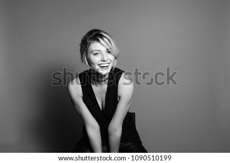 Close up studio portrait of a pretty blonde woman, laughing and looking at camera, against plain studio background