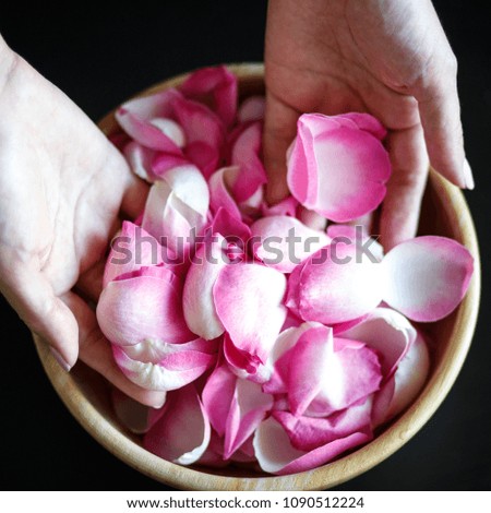 Close-up macro photo of woman's hands with rose petals, wooden bowl on a black table