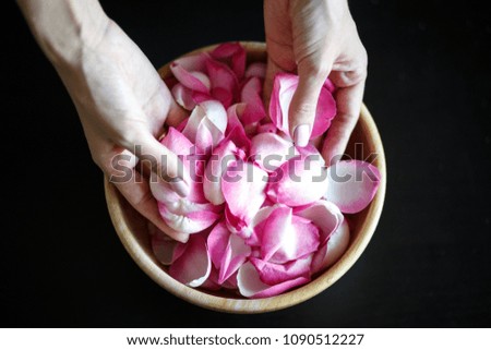 Close-up macro photo of woman's hands with rose petals, wooden bowl on a black table