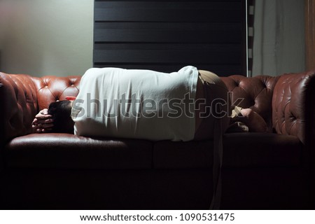 Abstract emotional picture of sad man. Unsuccessful people. Man feels disappointed in life. Man sleeps on the vintage leather sofa alone in living room.