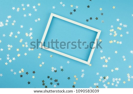 White picture frame and sequins stars on blue background. Top view, flat lay. Mockup for party or birthday invitation.