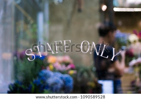 Staff only sign on window with blurry background of florist working in floral shop