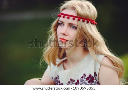tender blonde woman sits on the grass dressed in a natural embroidered dress bandage on her head, on a green background stylish and cozy. The concept of advertising the love of nature. place for text.