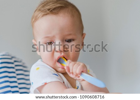 Small child sits on a chair and eating with spoon. Little baby are eating. Child sitting at empty table.Baby nutrition concept.Food advertisement design.