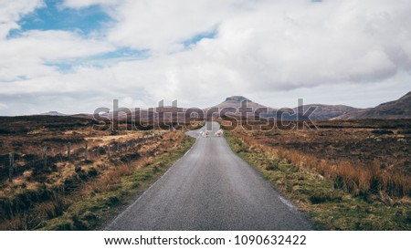 Sheep walking in the middle of a scottis road, with the typical Isle of Skye peaks in the background