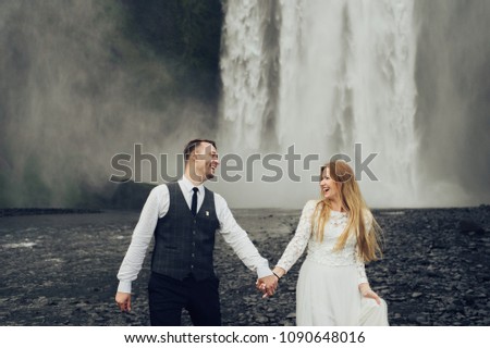 Iceland couple embrace near the big waterfall. Wall of the water on the background.