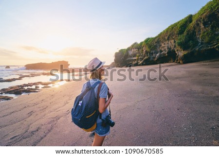 Traveling and photography. Young woman with camera and backpack walking by sea beach.