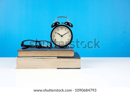 Education concept. An old book, eyeglasses and alarm clock over blue background