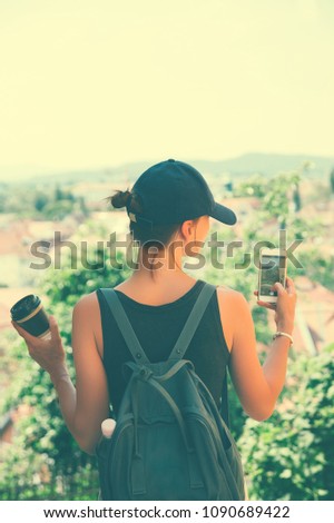 Woman tourist takes a picture panoramic view with red roofs of Ljubljana from Castle on smart phone. Girl traveler with backpack discovers Slovenia. Springtime or Summer in Europe. Travel and Vacation