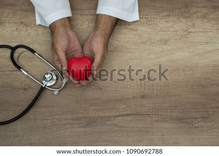 Hand of male doctor holding heart with stethoscope on the desk, closeup