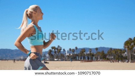 sport and healthy lifestyle concept - smiling young woman with fitness tracker running over venice beach background in california