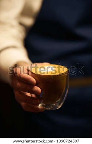 Barista in dark apron uniform holding a cup of coffee with latte art