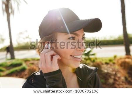 Photo of beautiful young sports lady outdoors in park listening music with earphones looking aside.