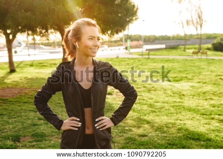 Photo of beautiful young sports lady outdoors in park listening music with earphones looking aside.