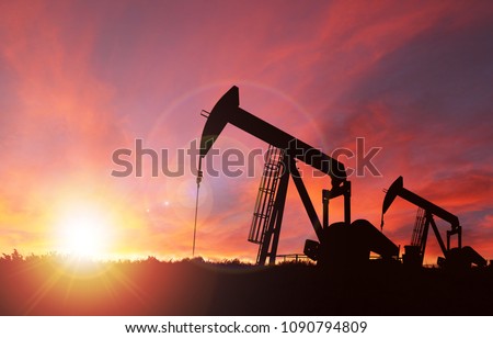 Pumpjack silhouette against a sunset sky with deliberate lens flare and copy space. These jacks can extract between 5 to 40 litres of crude oil and water emulsioin at each stroke.