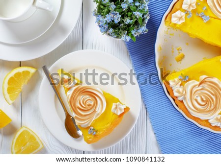 piece of Classic french lemon tart or Tarte au citron on a plate and in a baking dish with a custard lemon filling decorated with meringue roses and edible fresh flowers, view from above, close-up