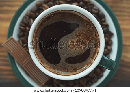Green cup with coffee on a saucer with coffee beans and a slice of chocolate. Background, wallpaper. Located by the middle