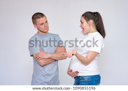family relationships. Portrait of young married couple: husband and pregnant wife communicate in studio on white background. They stand directly in front of the camera and show different emotions