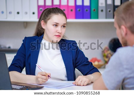 I am listening really carefully. Portrait of a brunette in the office taking a visitor at a table with a laptop. She sits right in front of the camera and talks to the client