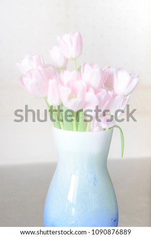 Pink tulip flowers in a blue vase by the window with soft sun light
