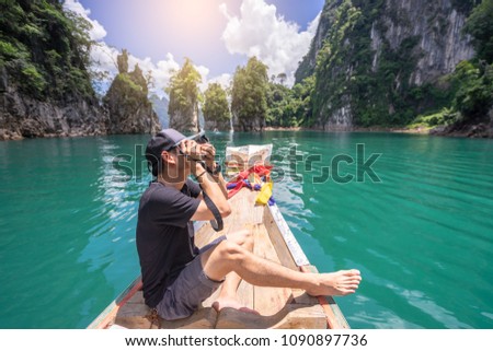Asians alone, taking pictures while on a wooden boat in the water happily on holiday.