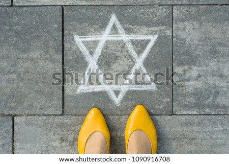Female feet with abstract image of a six-pointed star, written on grey sidewalk
