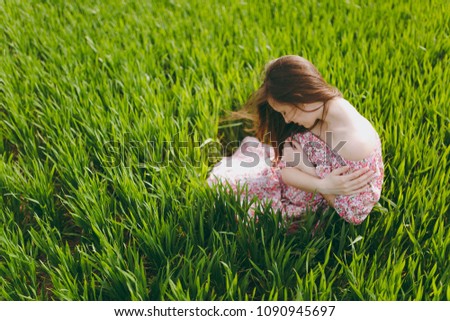 Young tender charming woman with closed eyes and lowered head in light patterned dress sitting on grass holding hands folded resting in sunny weather in field on green background. Lifestyle concept
