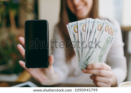 Close up photo of woman in coffee shop at table with bundle of dollars, cash money, mobile phone with blank empty screen to copy space, relaxing in restaurant during free time. Female rest in cafe