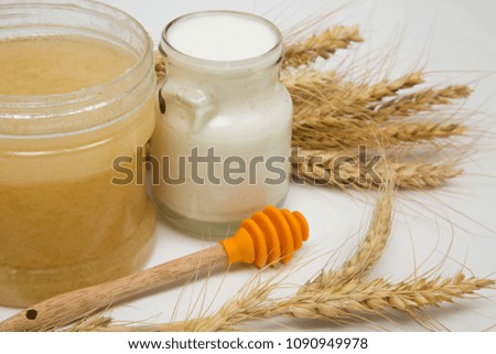 a frame of a honey jar with a honey dipper, a jar of milk and some Wheat stalks on a white background, Symbols of jewish holiday - Shavuot

