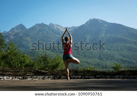 a woman is engaged in yoga in the mountains in the open area on the background of forested mountains. the tree pose. Vriksasana