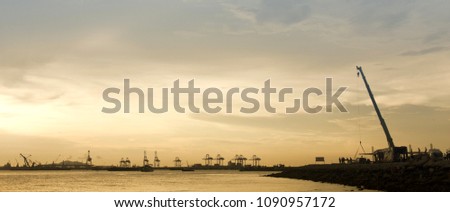 Panorama image Silhouette of construction site next to the sea in the sunset.