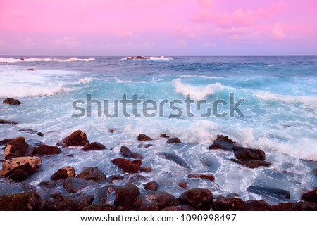 Beautiful pink tinted waves breaking on a rocky beach at sunrise on east coast of Big Island of Hawaii, USA