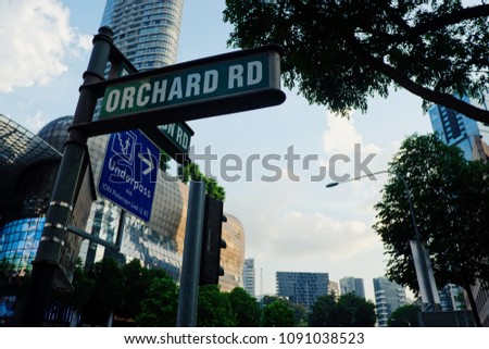 Eye-level view shot closeups of Street signs calls Orchard Rd, Singapore in the afternoon clear sky with branch tree be high the building town.