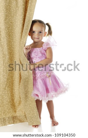 An adorable preschooler peeking from behind a curtain in her pink princess dress.  On a white background.