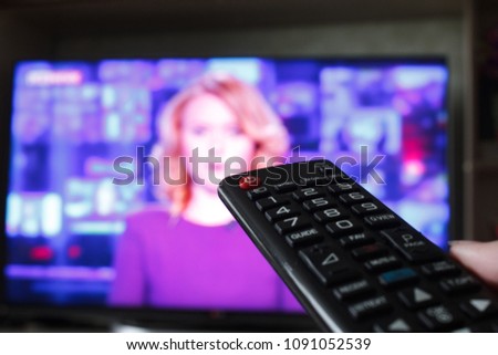 Close up Hand holding TV remote control with a television in the background. Royalty-Free Stock Photo #1091052539