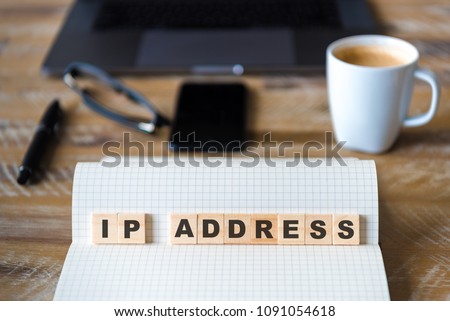 Closeup on notebook over wood table background, focus on wooden blocks with letters making IP ADDRESS words. Business concept image. Laptop, glasses, pen and mobile phone in a defocused background.