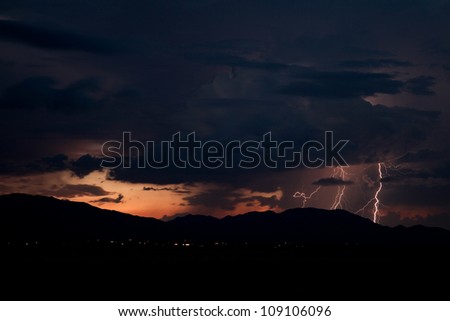 Spooky dramatic distant long narrow window shows dangerous cloud-to-ground lightning strikes at red and orange color twilight, between black sinister heavy sky and black dark nighttime background 