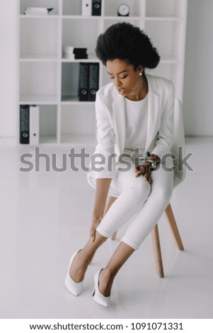 attractive african american businesswoman touching ankle in office