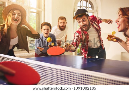 Group of happy young friends playing ping pong table tennis at office or any room. Concept of healthy sport and genuine emotions. Lifestyle, rest concepts Royalty-Free Stock Photo #1091082185